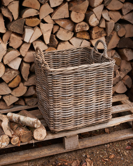 handmade  weaved rattan log basket in front of wood pile. 